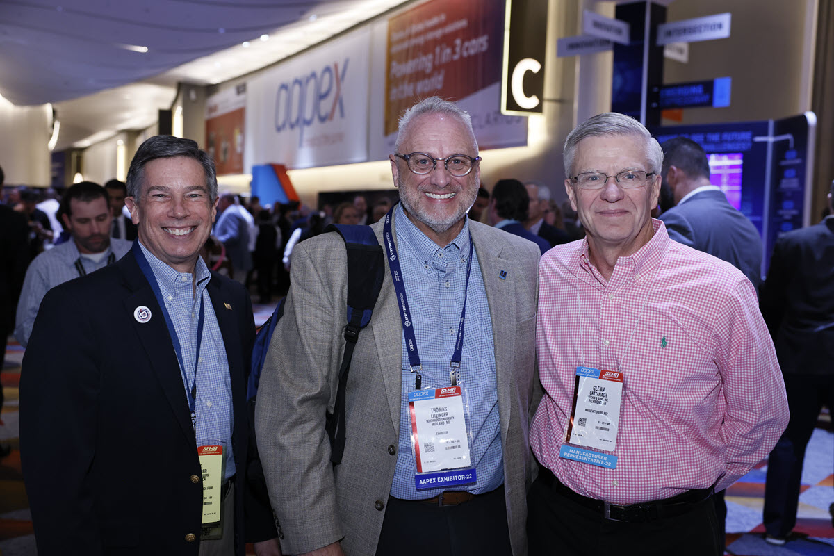 Three attendees smile in the AAPEX hall entrance